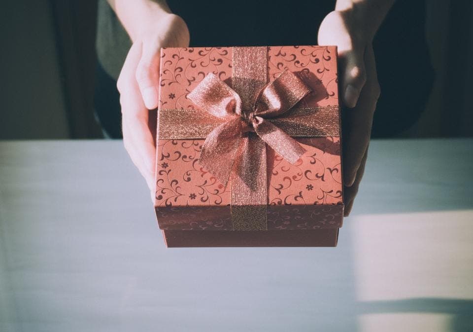 Hai bàn tay đưa ra một hộp quà thắt nơ màu hồng đất