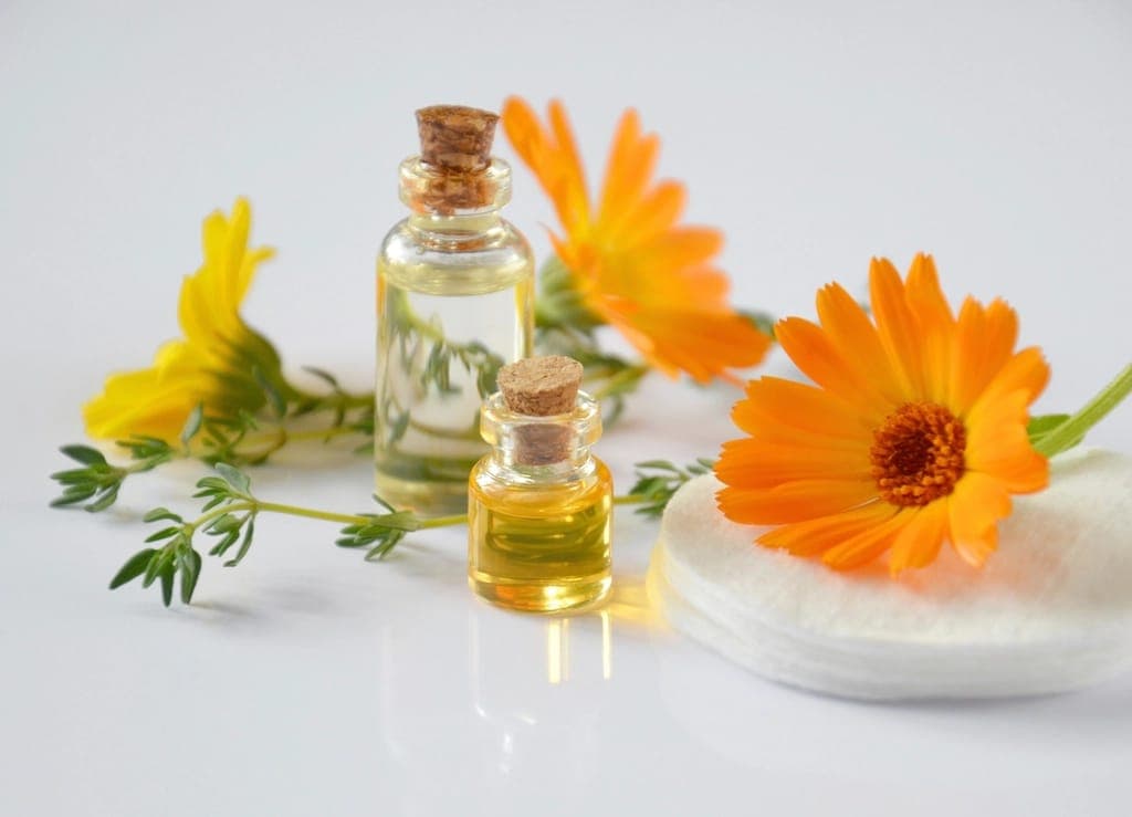 Lọ thuỷ tinh nhỏ đựng dầu bên hoa cúc vạn thọ và bông tẩy trang