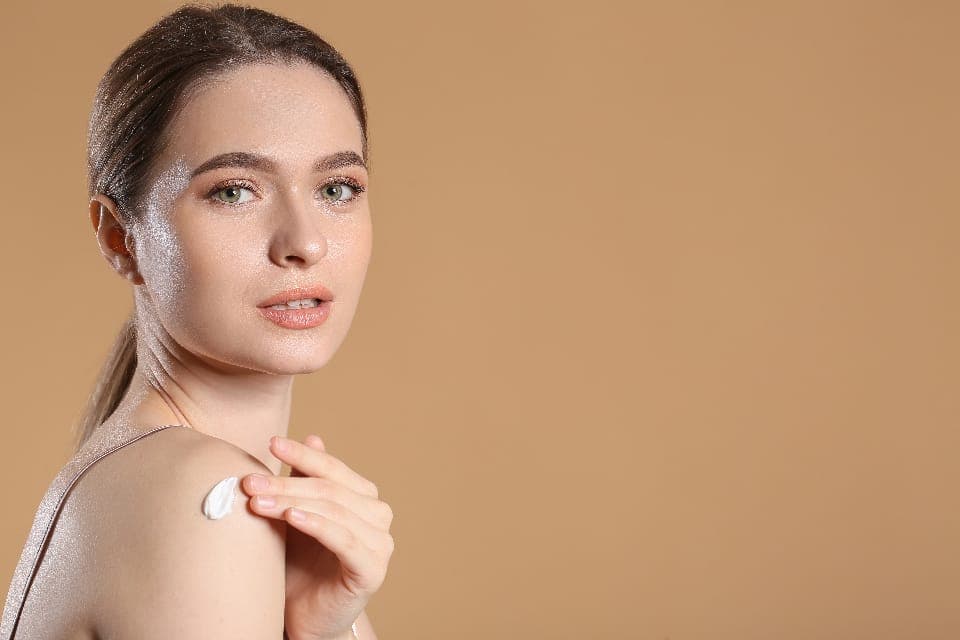 Người phụ nữ thoa kem lên bờ vai, nền màu be