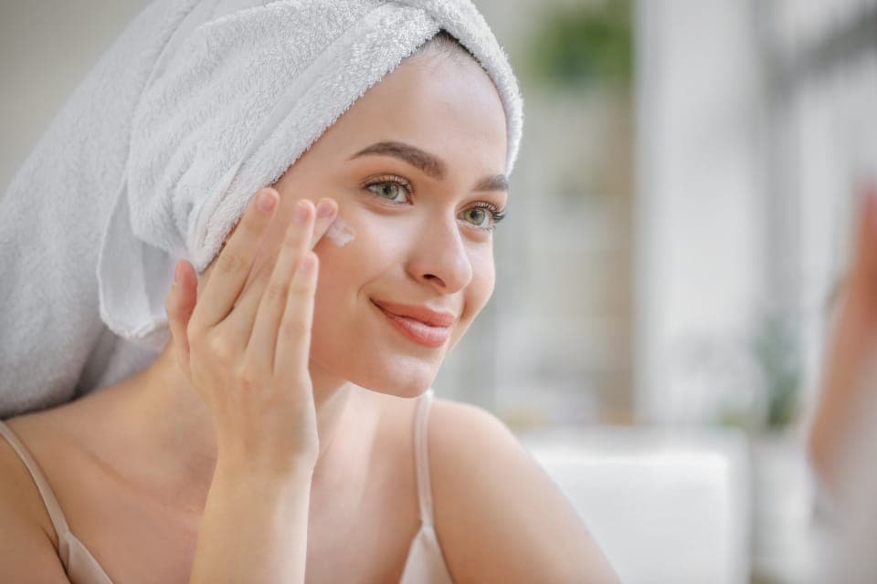 Người phụ nữ quấn khăn tóc thoa kem quanh mắt