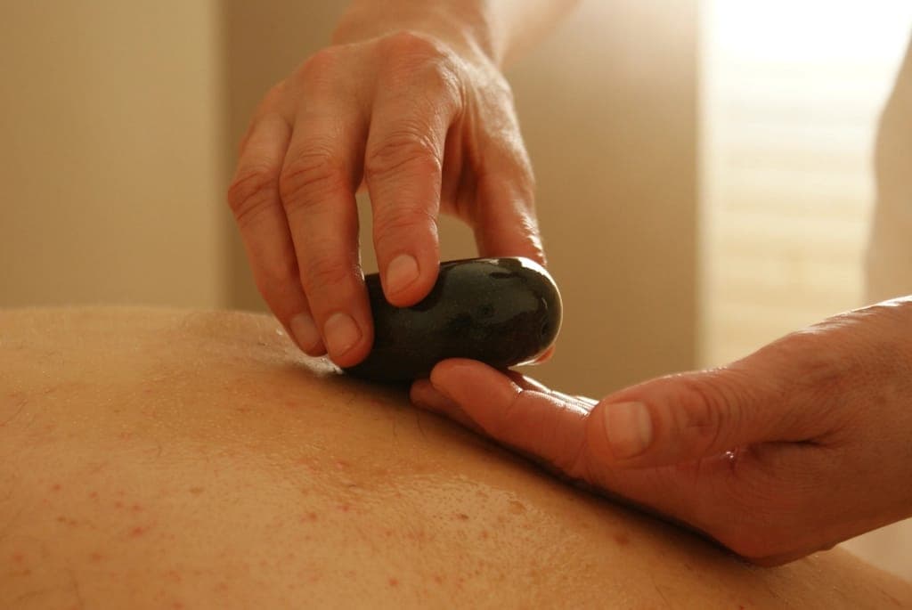 Tay kỹ thuật viên cầm viên đá nóng massage lưng