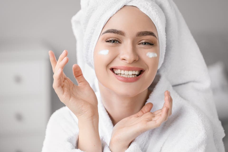 Người phụ nữ quấn khăn tóc, chấm kem trên má, cười tươi