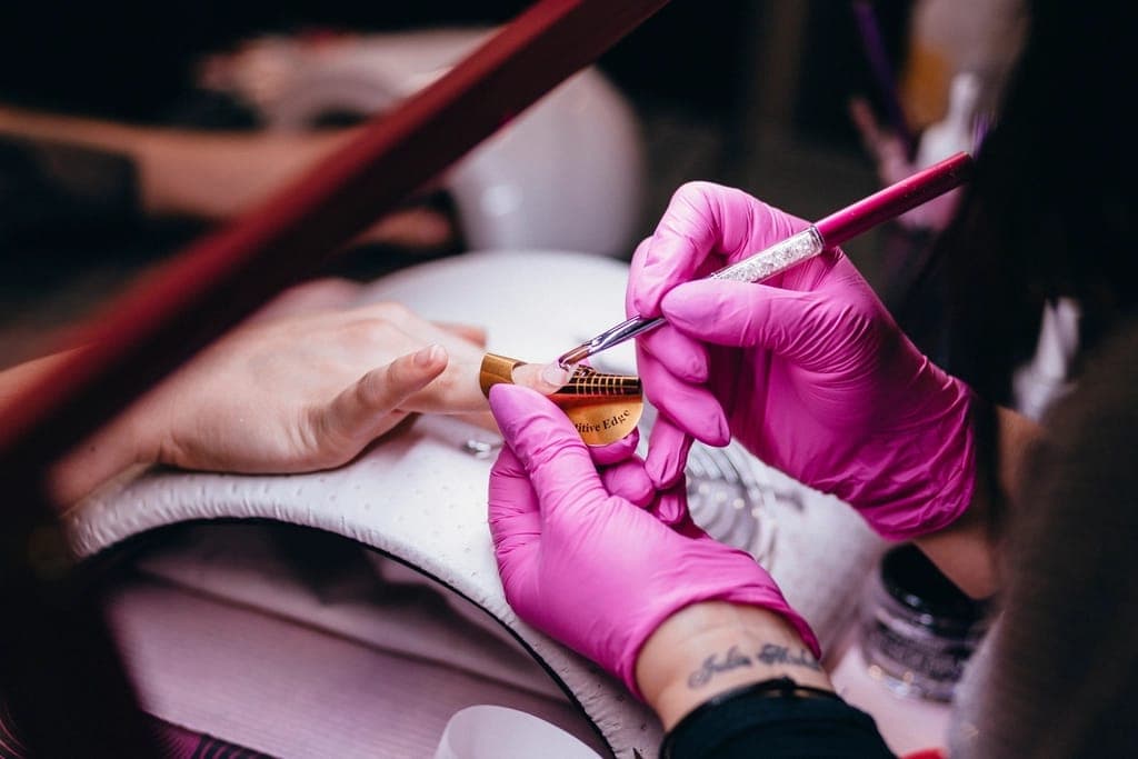 Thợ nail đeo găng hồng vẽ móng cho khách