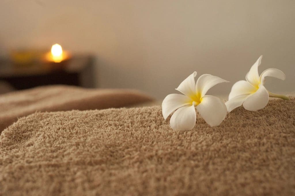 Hoa sứ trắng đặt trên khăn màu be, nến mờ phía sau