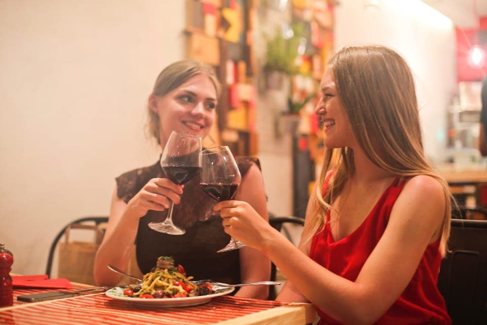 Hai người bạn nâng ly trò chuyện bên bàn ăn trong nhà hàng