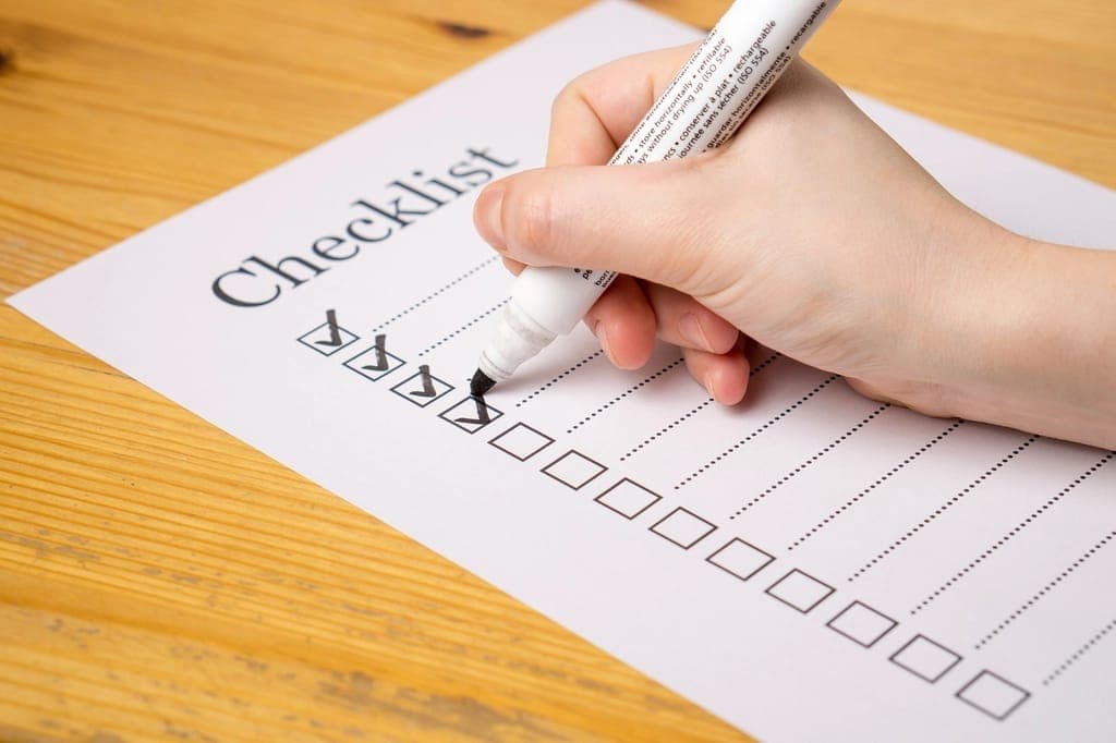 Bàn tay dùng bút dạ đánh dấu từng ô trên tờ checklist