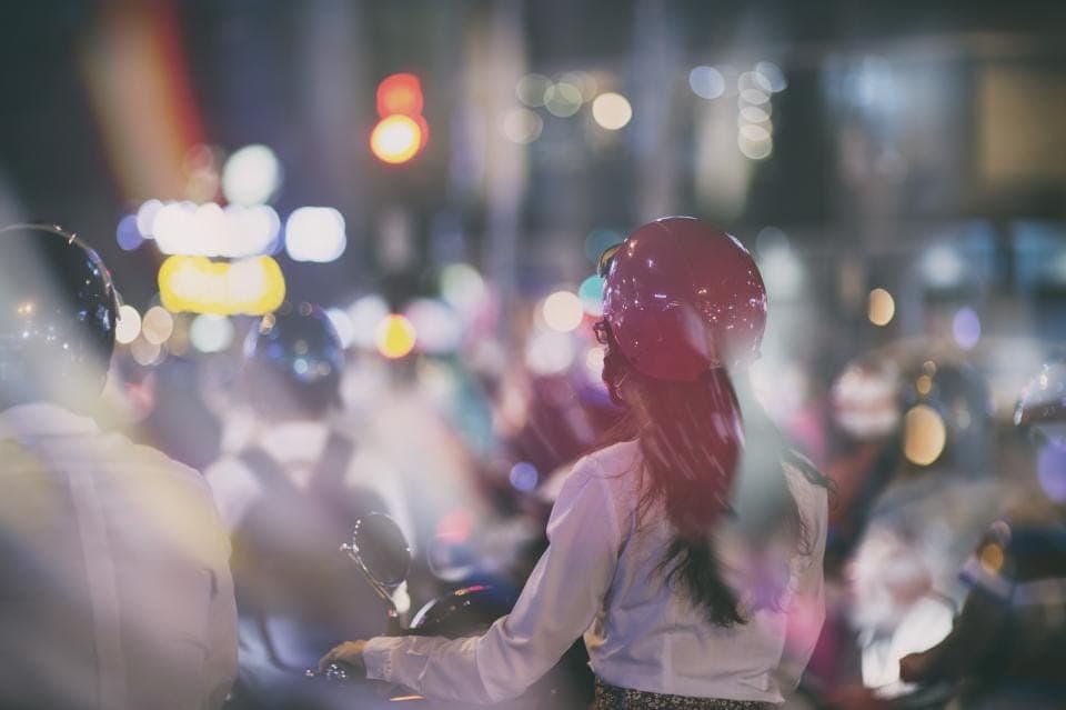 Người phụ nữ đội mũ bảo hiểm đỏ giữa dòng xe máy buổi tối