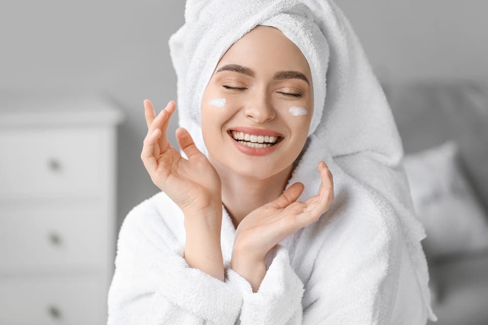 Người phụ nữ quấn khăn tóc, chấm kem trên má, nhắm mắt cười