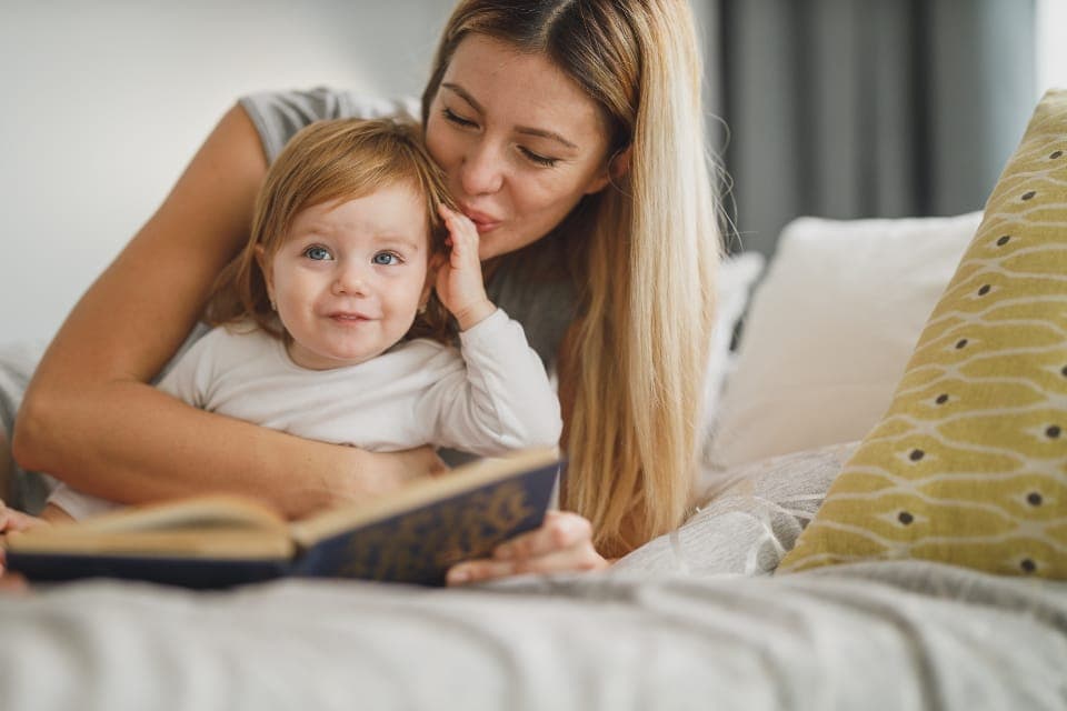 Mẹ ôm con nhỏ đọc sách trên giường