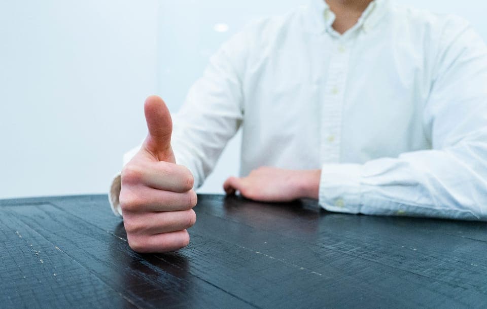 Người mặc áo sơ mi trắng giơ ngón cái bên bàn gỗ tối màu