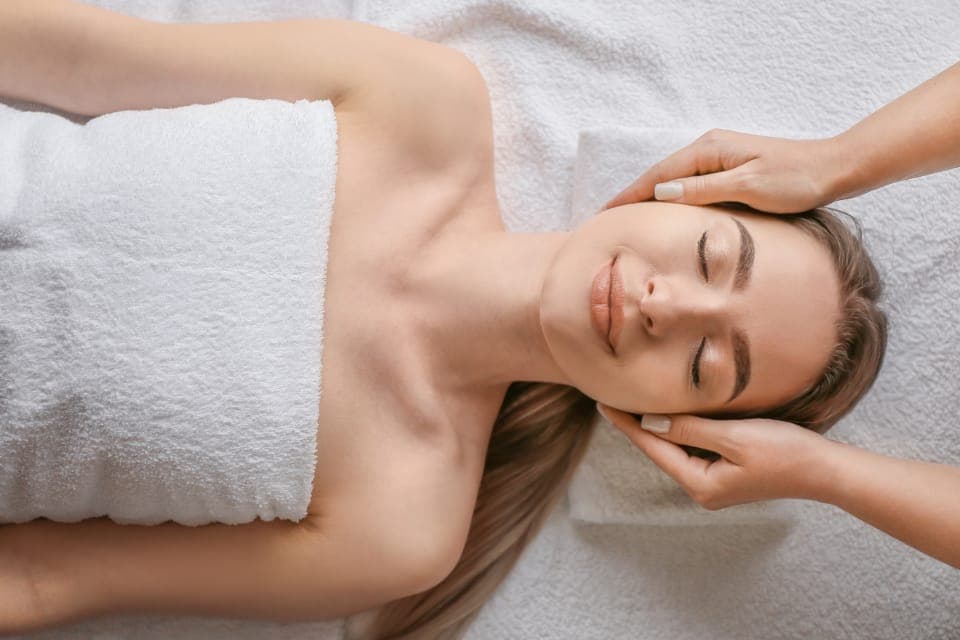 Khách nằm ngửa, quấn khăn trắng, được massage đầu