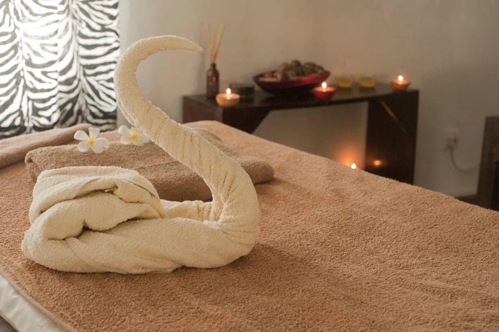 Khăn gấp hình thiên nga trên giường massage, nến thắp phía sau