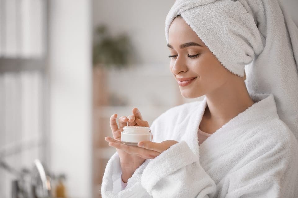 Người phụ nữ mặc áo choàng cầm hũ kem dưỡng