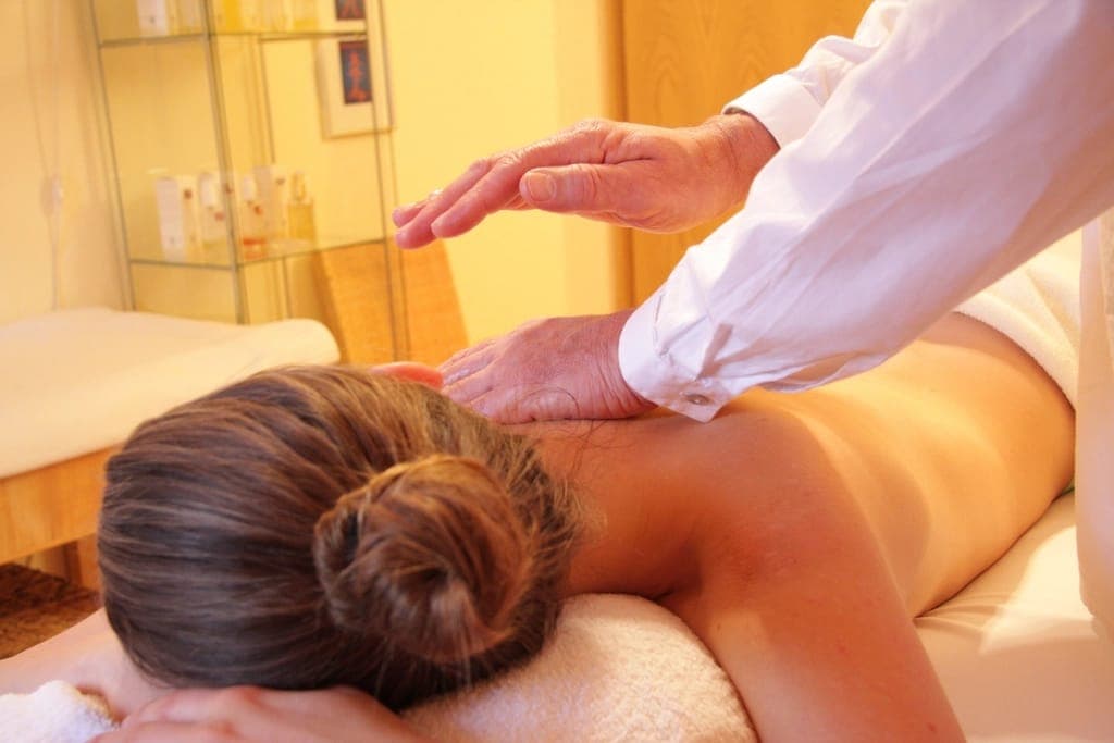 Kỹ thuật viên áo trắng đặt tay lên lưng người phụ nữ nằm sấp trên giường massage