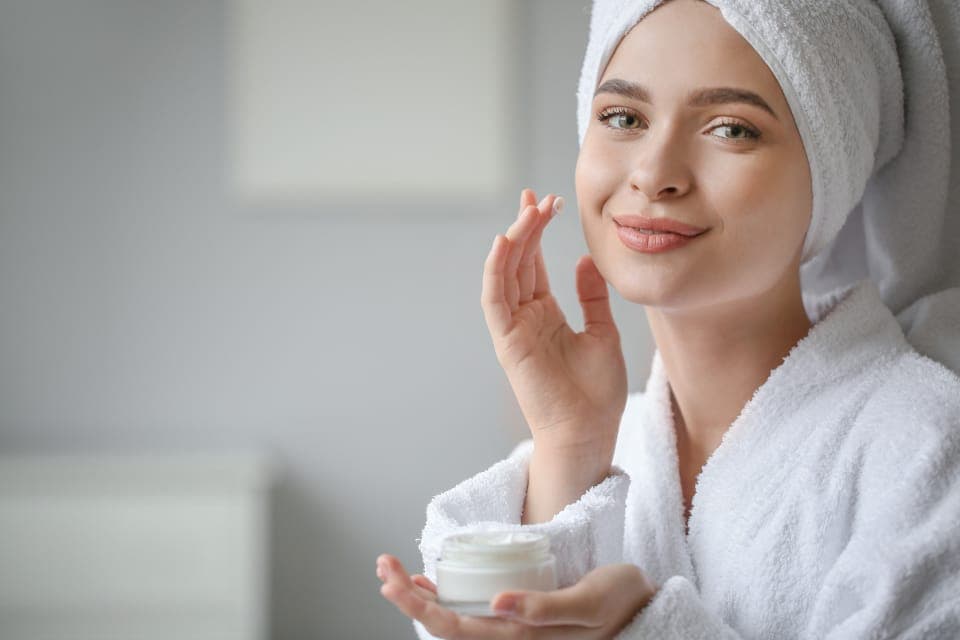 Người phụ nữ quấn khăn tóc thoa kem dưỡng lên mặt