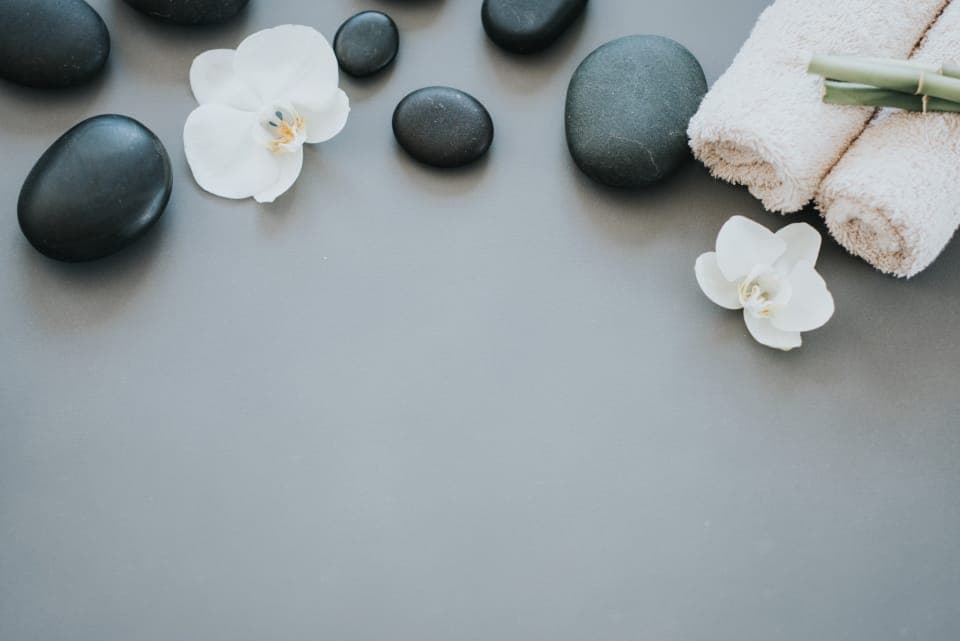 Đá đen, hoa lan trắng và khăn cuộn đặt trên nền xám