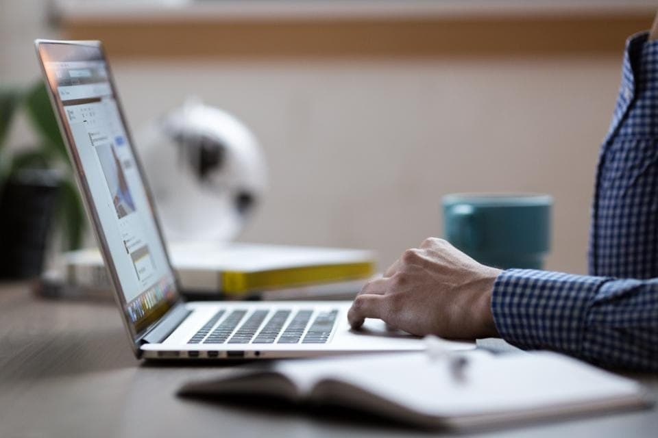 Người đàn ông áo sơ mi ca rô dùng laptop bên cốc và sổ tay
