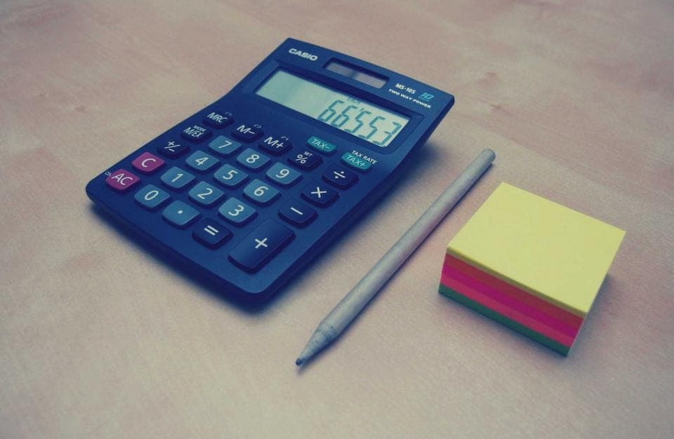 Máy tính cầm tay màu xanh, bút chì và tập giấy nhớ nhiều màu trên bàn
