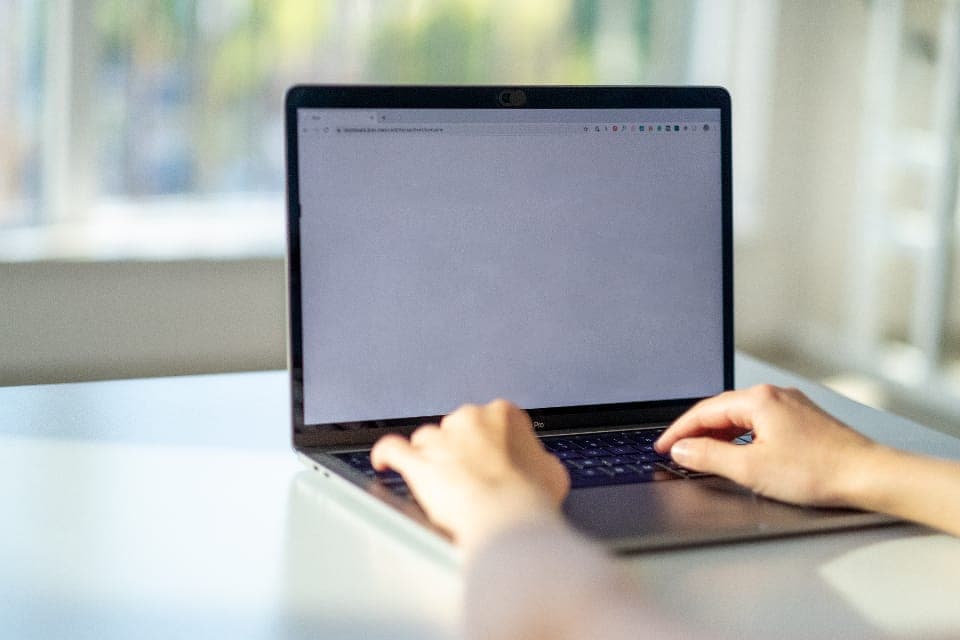 Hai bàn tay gõ phím laptop trên bàn trắng cạnh cửa sổ