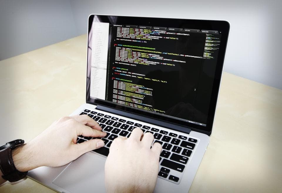 Hai bàn tay gõ phím trên laptop đang mở trình soạn mã