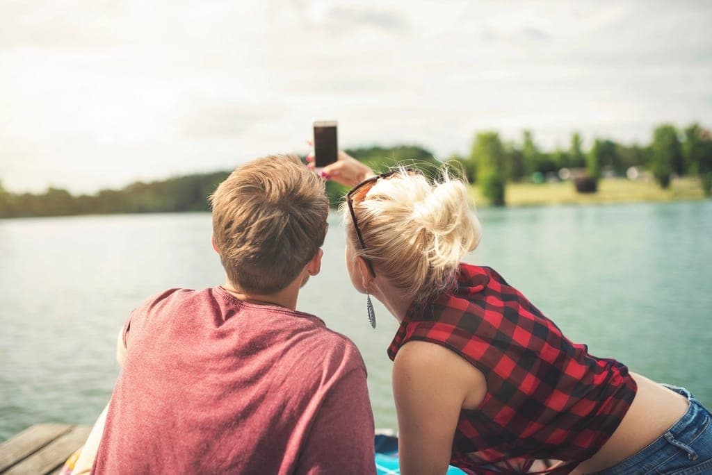 Hai người ngồi bên hồ chụp ảnh selfie