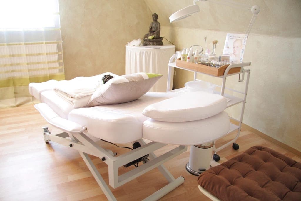 Phòng trị liệu với giường phủ khăn trắng, xe đẩy dụng cụ và đèn soi