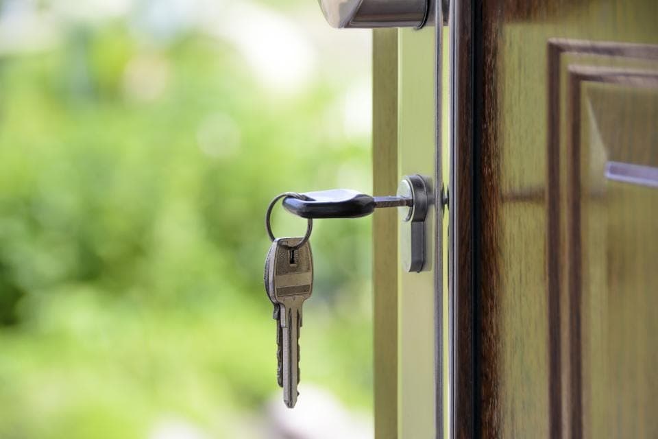 Chùm chìa khoá cắm trong ổ khoá cửa, phía sau là cây xanh