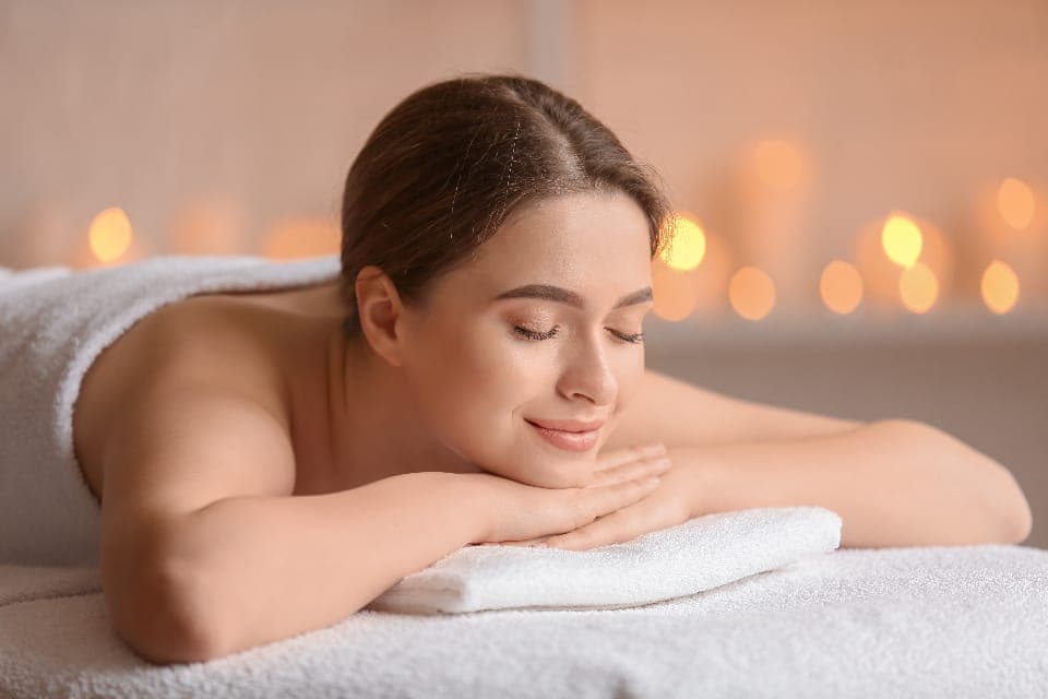Khách nằm sấp thư giãn trên giường spa, nền đèn nến mờ