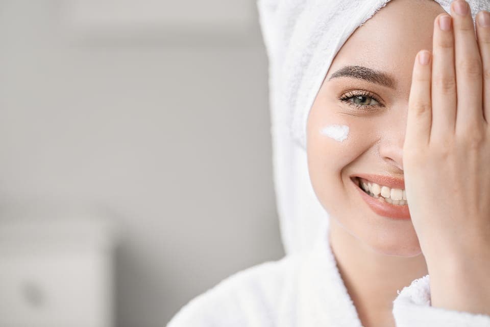 Người phụ nữ quấn khăn tóc, chấm kem trên má, che một mắt cười